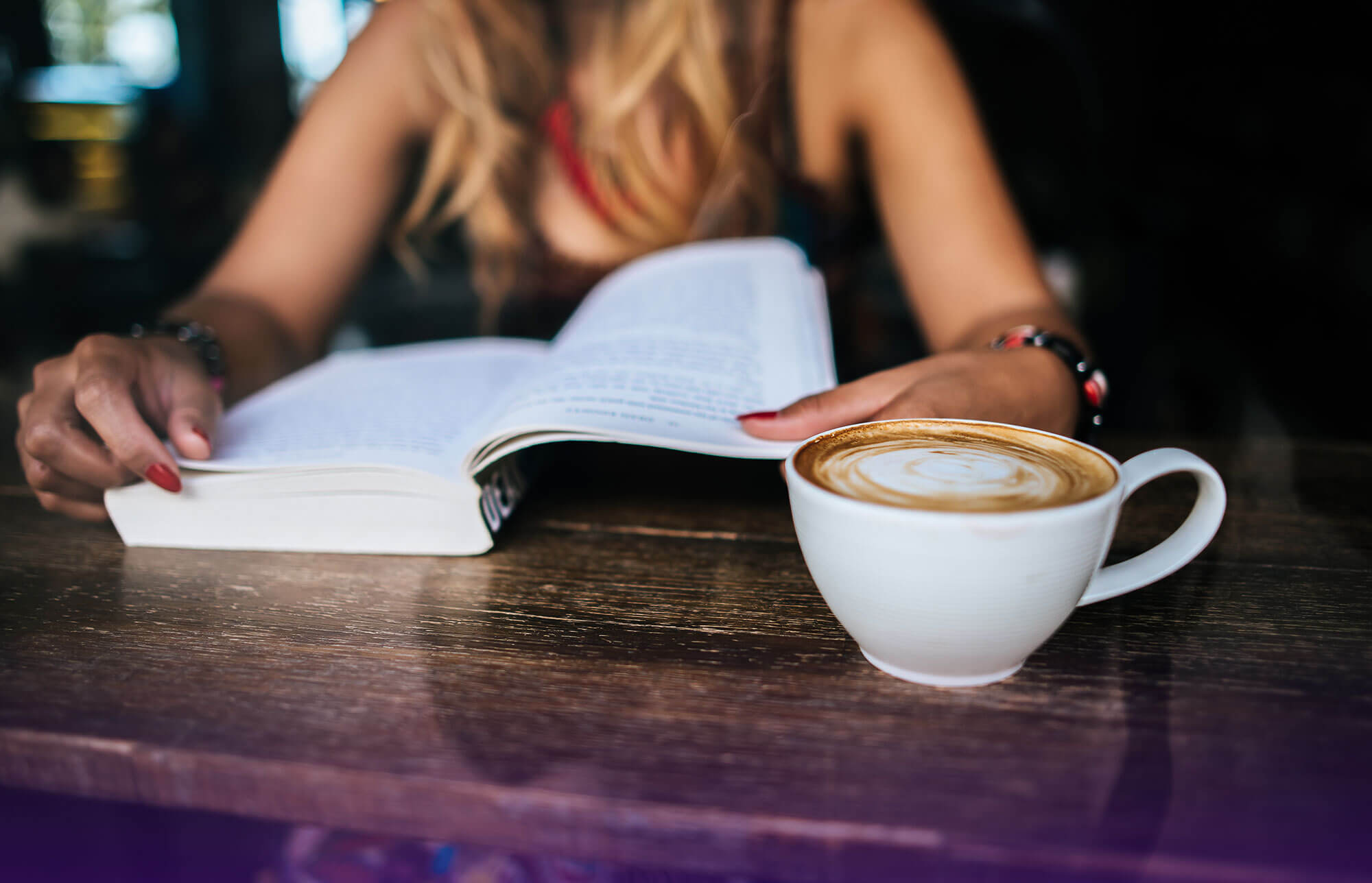Woman reading a book in a cozy coffee shop, embracing a positive money mindset and personal growth image
